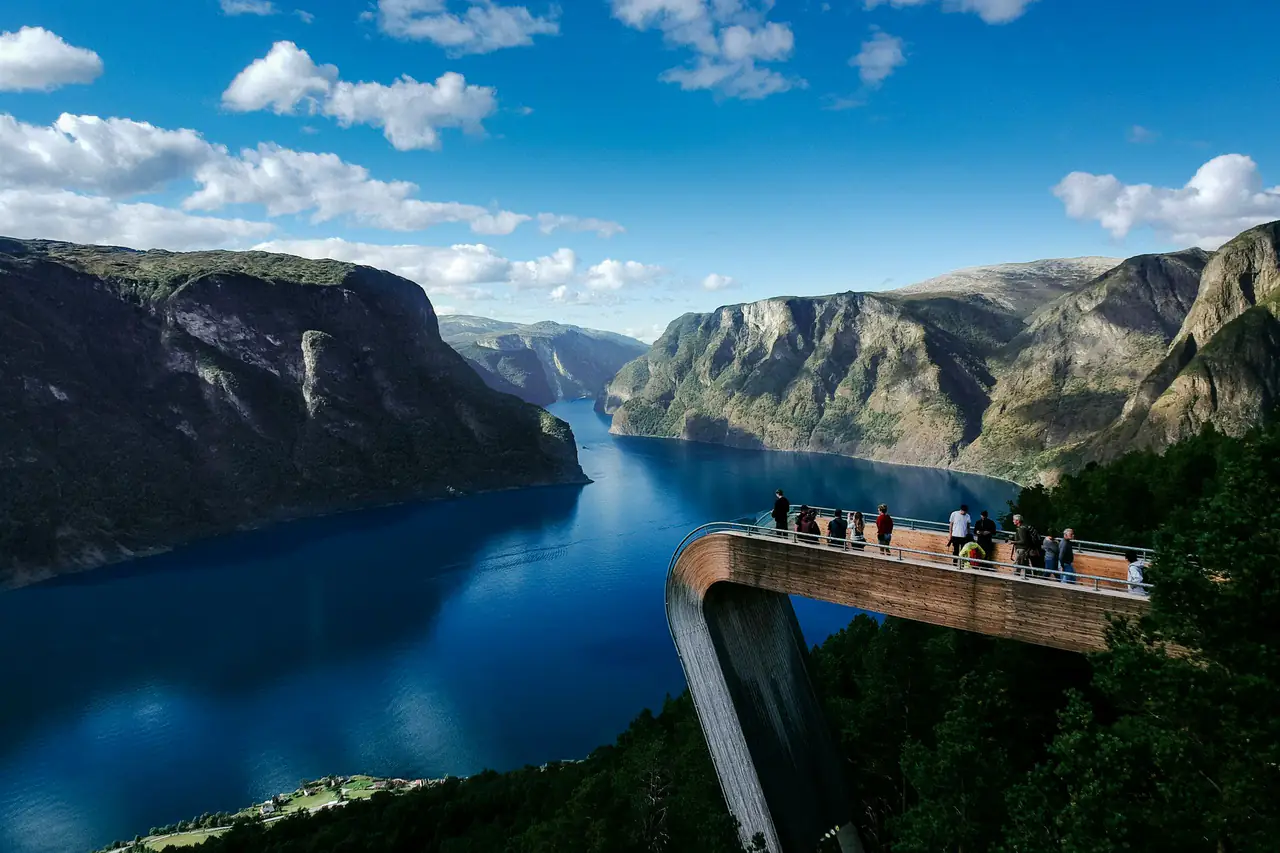 Travellers on a viewing platform high above a deep blue fjord